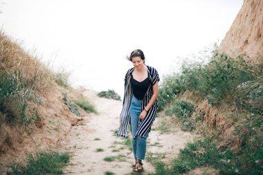 Şık hipster kız çim ile kumlu kayalıklar arasında yürüyüş