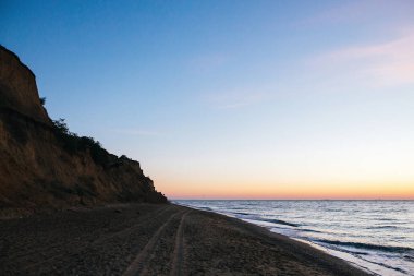 Güzel kumlu uçurum ve pembe gökyüzü ile güneş deniz dalgaları üzerinde doğuruyor