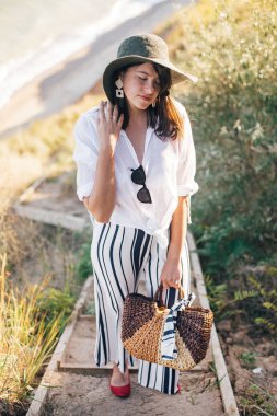 Şık boho kız şapka s yakın çim ile kumlu uçurumda poz