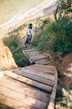 Şık boho kız s çim ile kumlu uçurumda ayakta şapka