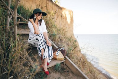 Güneşli ışıkta ahşap merdivenlerde oturan şapkaşık boho kız