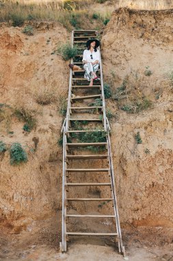 Şapka şık boho kız büyük kumlu c ahşap merdivenlerde oturan