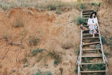 Şapka şık boho kız büyük kumlu c ahşap merdivenlerde oturan