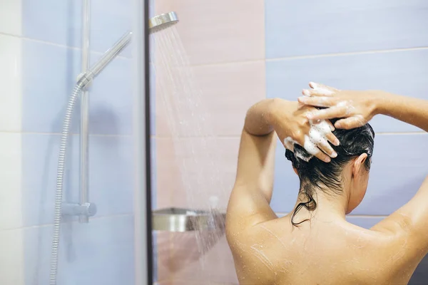 Молода щаслива жінка миє волосся шампунем, піниться з ха — стокове фото