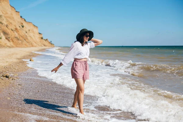 Stylisches Hipster-Mädchen mit Hut, das am Strand spazieren geht und lächelt. Sommer — Stockfoto