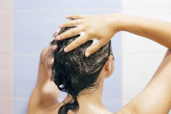 Молодая счастливая женщина моет волосы шампунем, руки пеной — стоковое фото