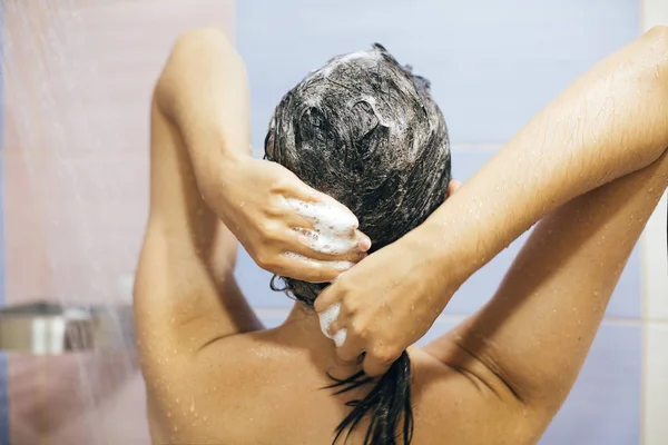 Junge glückliche Frau wäscht sich die Haare mit Shampoo, die Hände mit Schaum — Stockfoto