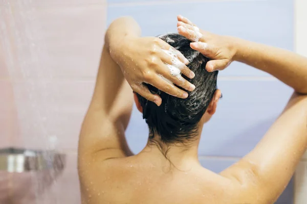 Молода щаслива жінка миє волосся шампунем, руки з піною — стокове фото