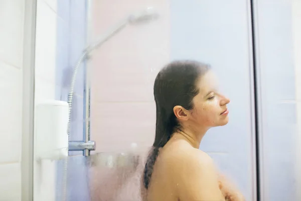 若い幸せな女性が家やホテルのバスルームで熱いシャワーを浴びています。S — ストック写真