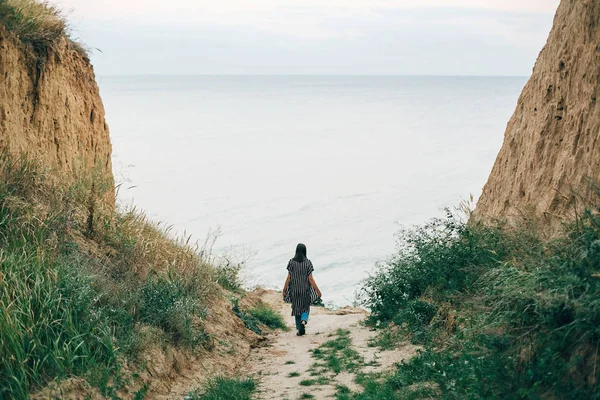 Menina hipster elegante andando para o mar entre penhascos arenosos com gr — Fotografia de Stock