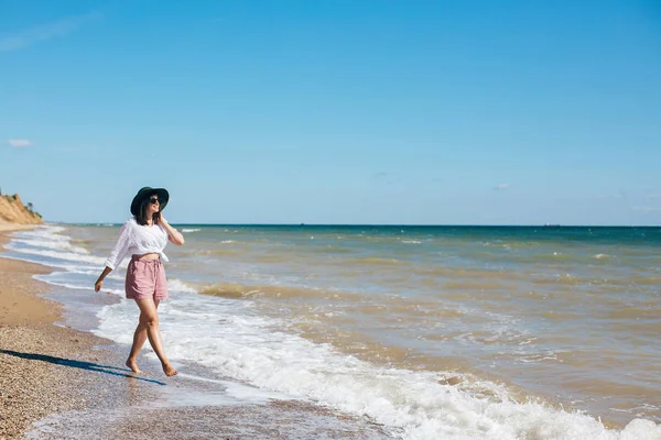 Stylisches Hipster-Mädchen mit Hut, das am Strand spazieren geht und lächelt. Sommer — Stockfoto