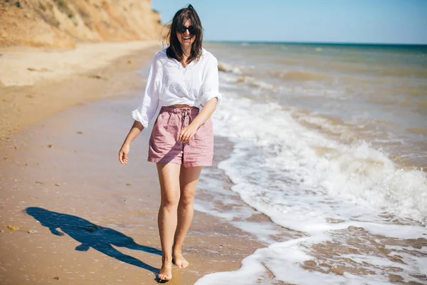 Stylisches Hipster-Mädchen, das am Strand spazieren geht und lächelt. Sommerurlaub — Stockfoto