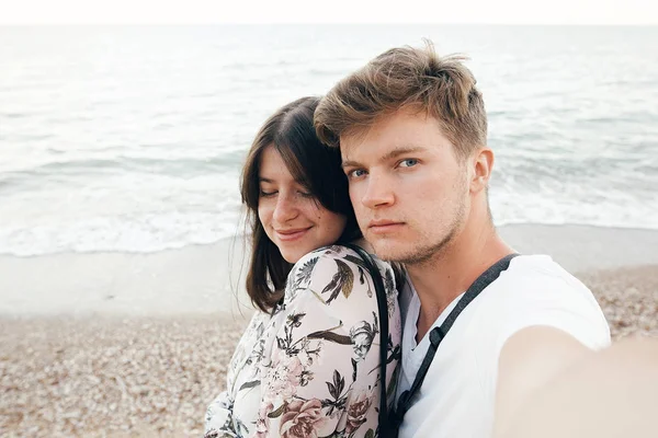 Stylish hipster couple taking selfie on beach at evening sea. Su — Stock Photo, Image