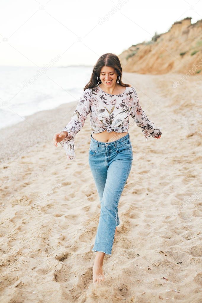 Stylish hipster girl running on beach at sea and smiling. Happy 