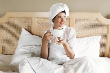 Güzel mutlu genç kadın kahve içme ve yatakta gülümseyen i