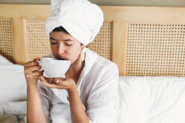 Otel odasında yatakta kahve içen güzel mutlu genç kadın