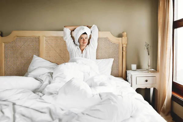 Красива щаслива молода жінка прокидається в ліжку з білими простирадлами — стокове фото