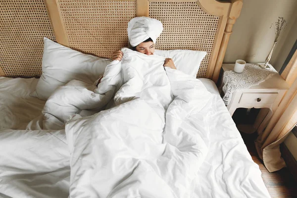 Beautiful happy young woman hiding under white sheets, lying on — Stock Photo, Image