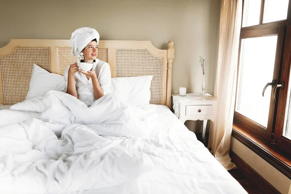 Красива щаслива молода жінка п'є каву і посміхається в ліжку я — стокове фото