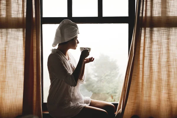 Mooie gelukkige jonge vrouw die koffie of thee drinkt, zittend op b — Stockfoto