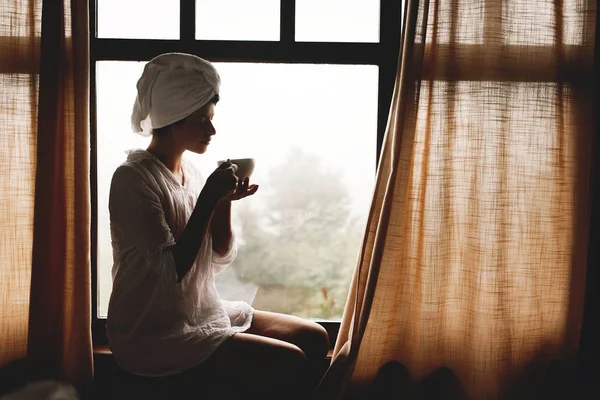 Mooie gelukkige jonge vrouw die koffie of thee drinkt, zittend op b — Stockfoto