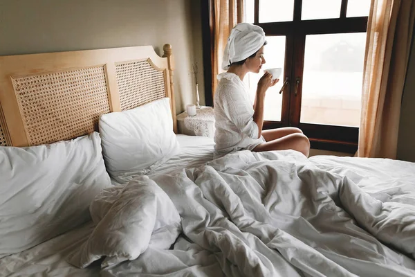 Hermosa joven feliz bebiendo café o té en la cama en caliente —  Fotos de Stock