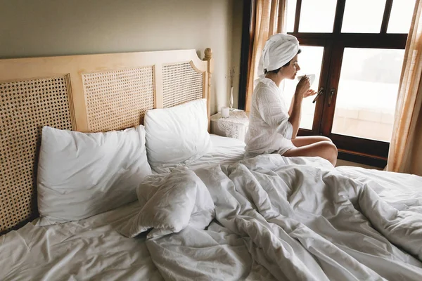 Hermosa joven feliz bebiendo café en la cama en la habitación de hotel —  Fotos de Stock