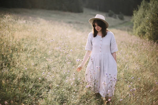 Stylish girl in linen dress walking among wildflowers in sunny m — Stock Photo, Image