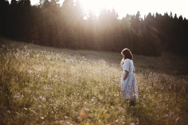 Стильная девушка в льняном платье, гуляющая среди полевых цветов в солнечных лучах — стоковое фото
