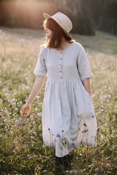 Stílusos lány rusztikus ruhában séta vadvirágok a napfényes MEA — Stock Fotó