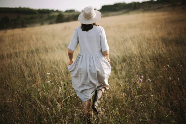 Elegante ragazza in abito di lino in esecuzione tra erbe e fiori selvatici — Foto Stock