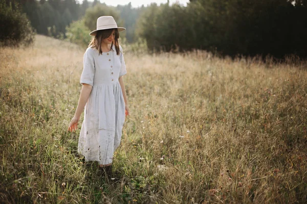 Stijlvolle meisje in linnen jurk wandelen tussen kruiden en wilde bloemen — Stockfoto