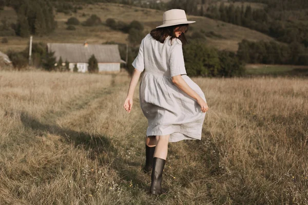 Menina elegante em vestido de linho e chapéu correndo na grama campo ensolarado — Fotografia de Stock