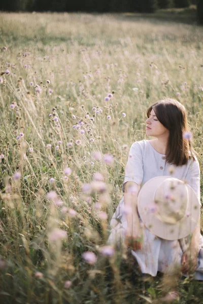 Stílusos lány rusztikus ruhában ülve között vadvirágok és gyógynövények — Stock Fotó