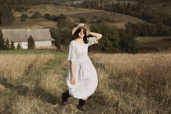 Stylish girl in linen dress and hat running and smiling in sunny