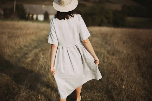 Chica con estilo en vestido de lino y sombrero caminando descalzo entre hierbas —  Fotos de Stock