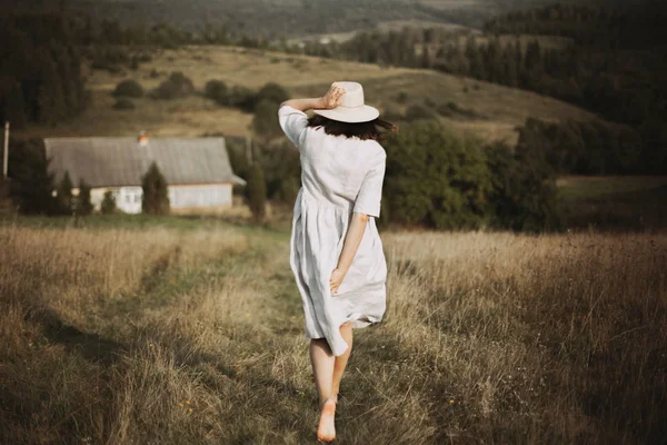 Chica con estilo en vestido de lino y sombrero corriendo descalzo en la hierba en — Foto de Stock