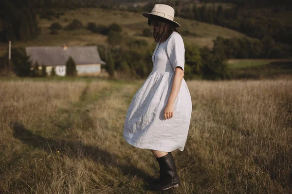 Elegante chica en vestido de lino y sombrero caminando entre hierbas y salvajes —  Fotos de Stock