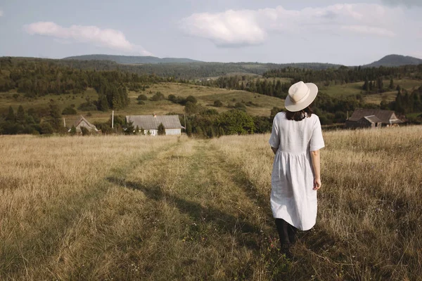 Chica con estilo en vestido de lino y sombrero caminando en la hierba del campo soleado — Foto de Stock