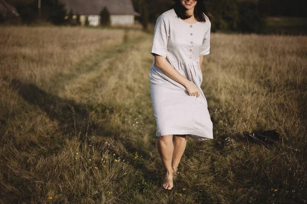 Stylish girl in linen dress and hat running barefoot in grass in — Stock Photo, Image