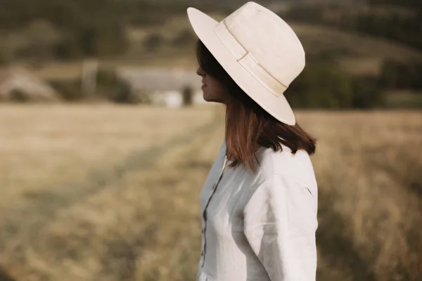 Stylish girl in linen dress and hat walking in sunny field grass — Stock Photo, Image