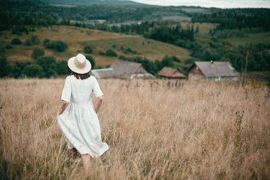 Keten elbise ve şapka otlar ve vahşi arasında yürüyüş şık kız