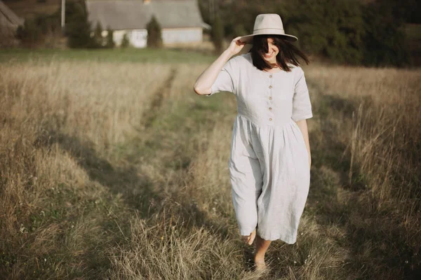 Стильная девушка в льняном платье и шляпе шагает бароножкой среди трав — стоковое фото