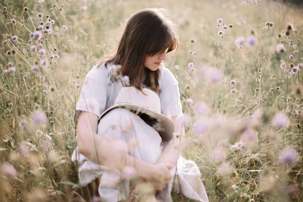 Stylová dívka v rustikálním oblečení a klobouku, které sedí mezi květinami a — Stock fotografie