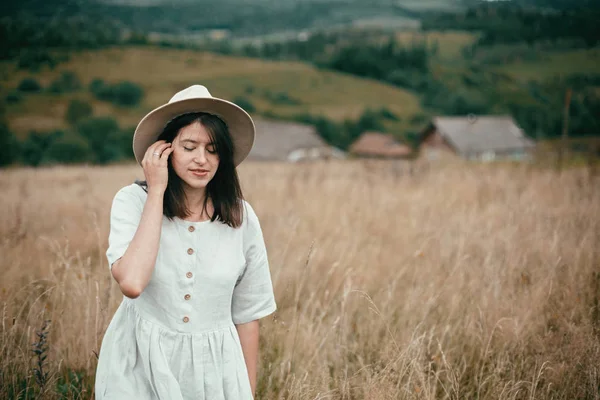 Gadis bergaya dengan gaun linen dan topi berjalan di antara tanaman herbal dan liar — Stok Foto