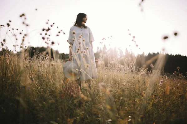 Stylish girl in rustic dress standing among wildflowers and herb