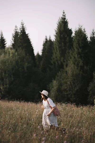 时尚的女孩在质朴的礼服和帽子走在野花之间 — 图库照片
