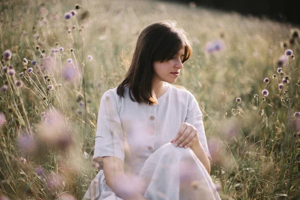 Стильна дівчина в сільському вбранні, що сидить серед диких квітів і трав — стокове фото