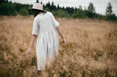 Keten elbise ve şapka otlar ve vahşi arasında yürüyüş şık kız