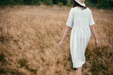 Keten elbise ve şapka otlar ve vahşi arasında yürüyüş şık kız